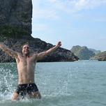 Man joyfully splashing water while standing in the sea with scenic cliffs in the background.
